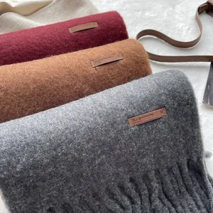 Close-up of brushed wool scarves in burgundy, camel and grey with fringe and leather tags