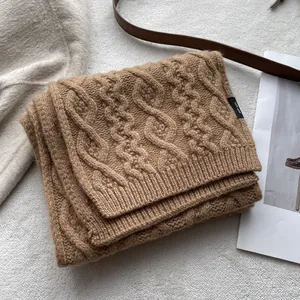Detail of cable knit wool scarf in camel with a black label showing 100% wool material