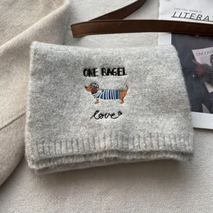 Detail of grey knitted scarf featuring embroidered dachshund and 'ONE BAGEL' text