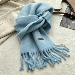 Detailed texture of light blue tassel scarf with a small brown leather label detail