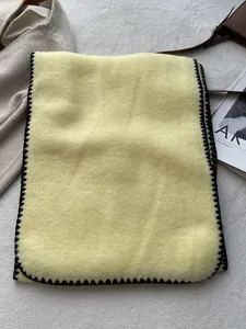 Detailed close-up of thick beige wool scarf with black whipstitch edge on textured carpet
