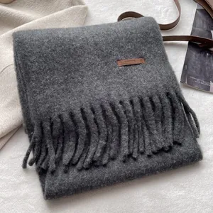 Close-up of dark grey wool scarf featuring long tassels and a brown leather patch
