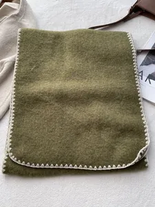 Detail of olive green wool scarf showing white blanket stitch edges and soft texture