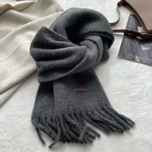 Detail of dark grey fringe scarf with leather label on soft textured fabric background