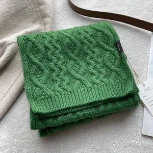 Detail view of green 100% merino wool scarf showing classic chunky cable knit and label