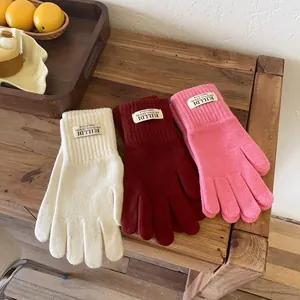 Close-up of three pairs of thick knitted touchscreen gloves in cream, red, and pink colors