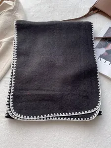 Detail of dark grey wool scarf with white blanket stitch edges on a plush background