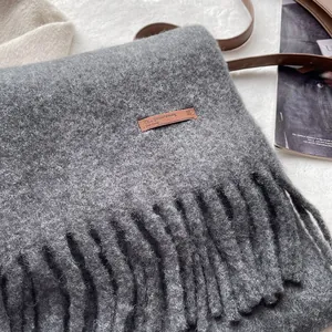 Close-up of grey wool scarf texture with thick tassels and premium leather brand label