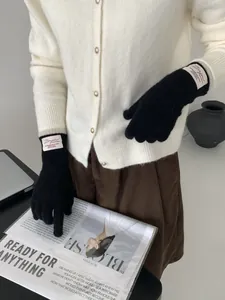 Dettaglio di guanti neri in maglia con etichetta in tessuto Bonjour e trama invernale