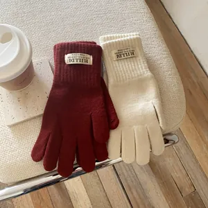 Close-up of winter knitted gloves in burgundy and cream with ribbed cuffs and woven labels