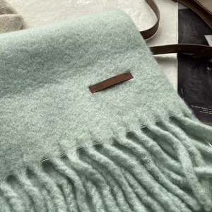Detailed macro view of mint green fuzzy scarf with leather label and thick tassels