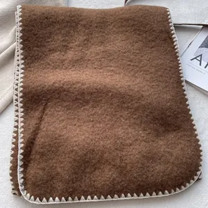 Thick dark brown wool scarf with white blanket stitch edges in a cozy winter setting