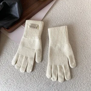 Close-up of cream-colored knit gloves with ribbed cuffs and embroidery on plush background