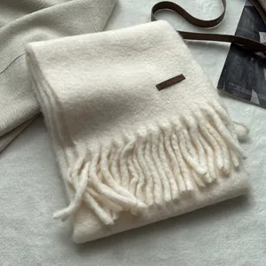 Detail of cream tassel scarf with wool-like texture and brown decorative label