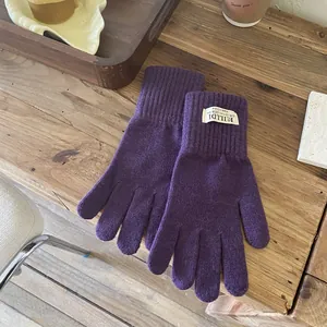 Close-up of deep purple knitted gloves with ribbed cuffs and woven label detail