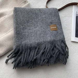 Detailed close-up of dark grey wool blend scarf with fringe edges and leather logo patch
