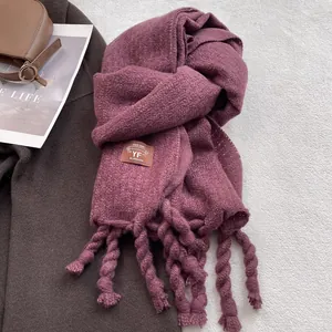 Detalle de bufanda gruesa de color púrpura oscuro con borlas y etiqueta de marca