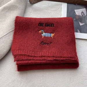 Detail of red knit scarf with dachshund embroidery and ONE BAGEL lettering text
