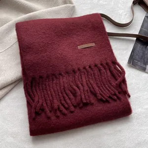 Detailed macro view of burgundy knit scarf with brown leather label and twisted tassels