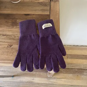 Detail of purple knitted touchscreen gloves with ribbed cuffs on a rustic wooden surface