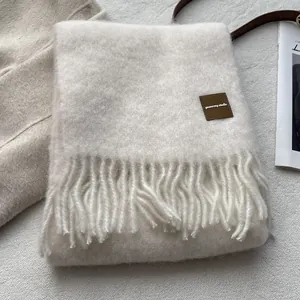 Detail of off-white wool blend scarf showing soft texture, fringe edges and leather tag