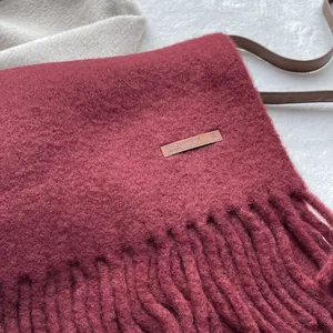 Close-up of deep wine red wool scarf texture with elegant tassels and leather label