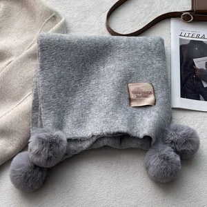 Detail of grey knitted scarf with soft pom-poms and a vintage woven label on its surface