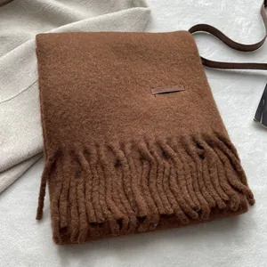 Close-up of dark brown wool scarf with thick tassels and premium leather label detail