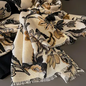 Detail of floral printed scarf with fringe edges in cream black and gold tones
