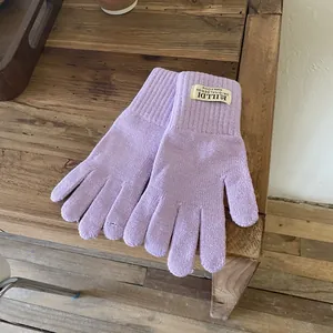 Detail of light purple knitted gloves with ribbed cuff and Hilldi logo label on wood