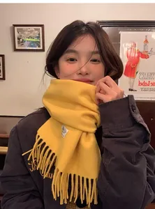 Détail d'une écharpe en laine jaune vif avec des franges douces et une étiquette tissée