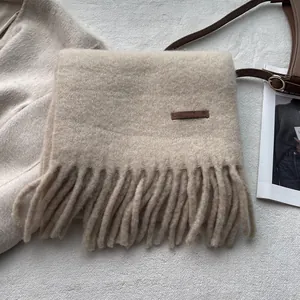 Close-up of beige knit scarf texture with fringe detail and brown leather brand label