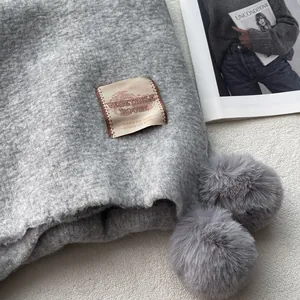 Close-up of gray knit scarf featuring pom-pom detail and a stylish textile brand label