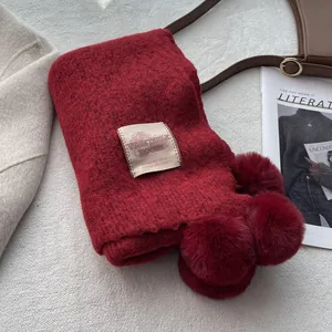 Detail of dark red knit scarf featuring four large plush pom-poms and brand label