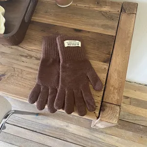 Close-up of winter knitted gloves in dark brown with branded woven cuff label on wood