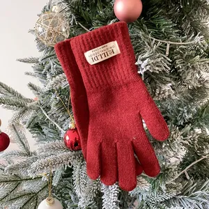 Close-up of red knitted winter gloves with logo patch on festive Christmas tree branches