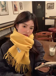 Détail de l'écharpe en laine jaune avec franges et étiquette dans un cadre café