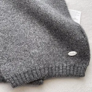 Close-up of deep gray knit scarf texture with a silver metal tag and ribbed edge detail