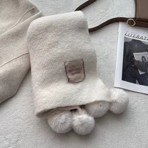 Detail of cream knit scarf featuring fluffy pom-poms and a vintage brown brand label