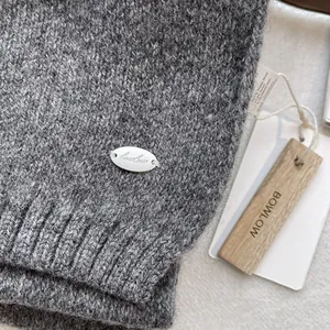 Detail of dark grey knit scarf featuring a silver metal logo tag and rustic wooden labels