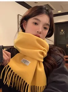 Détail d'une écharpe en laine jaune avec franges et étiquette sur un manteau sombre