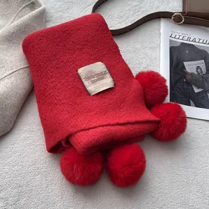 Detail of red knit scarf featuring soft pom-poms and a minimalist woven label