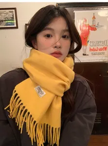 Détail d'une écharpe en pure laine jaune vif avec franges et étiquette de marque tissée