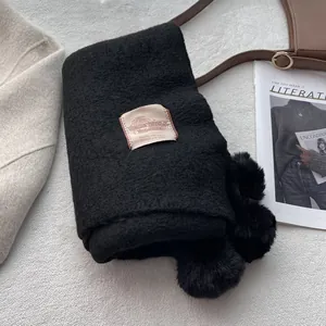 Detail of black faux cashmere scarf featuring plush pom-poms and minimalist woven label