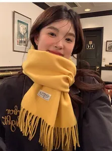 Détail de l'écharpe en laine jaune vif avec bords à franges et étiquette tissée