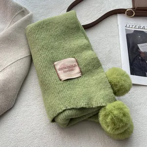 Detail of green knitted scarf with pom-pom trim and Vegetable House brand label