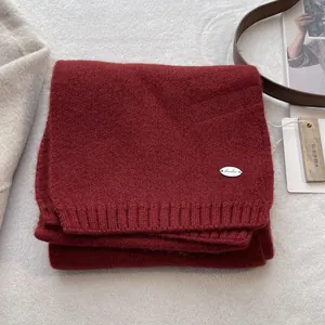 Detail of dark red knit scarf featuring silver metal logo tag and cedar wood tag