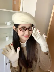 Detail of cream-colored knit flip-top gloves with red embroidery on a female model
