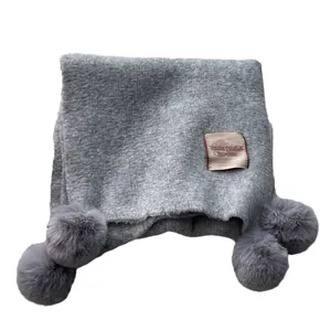 Grey knit scarf with plush pom poms and vintage woven label on white background