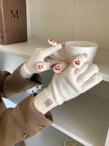 Close-up of cream knitted fingerless gloves with red smile embroidery and flip cover